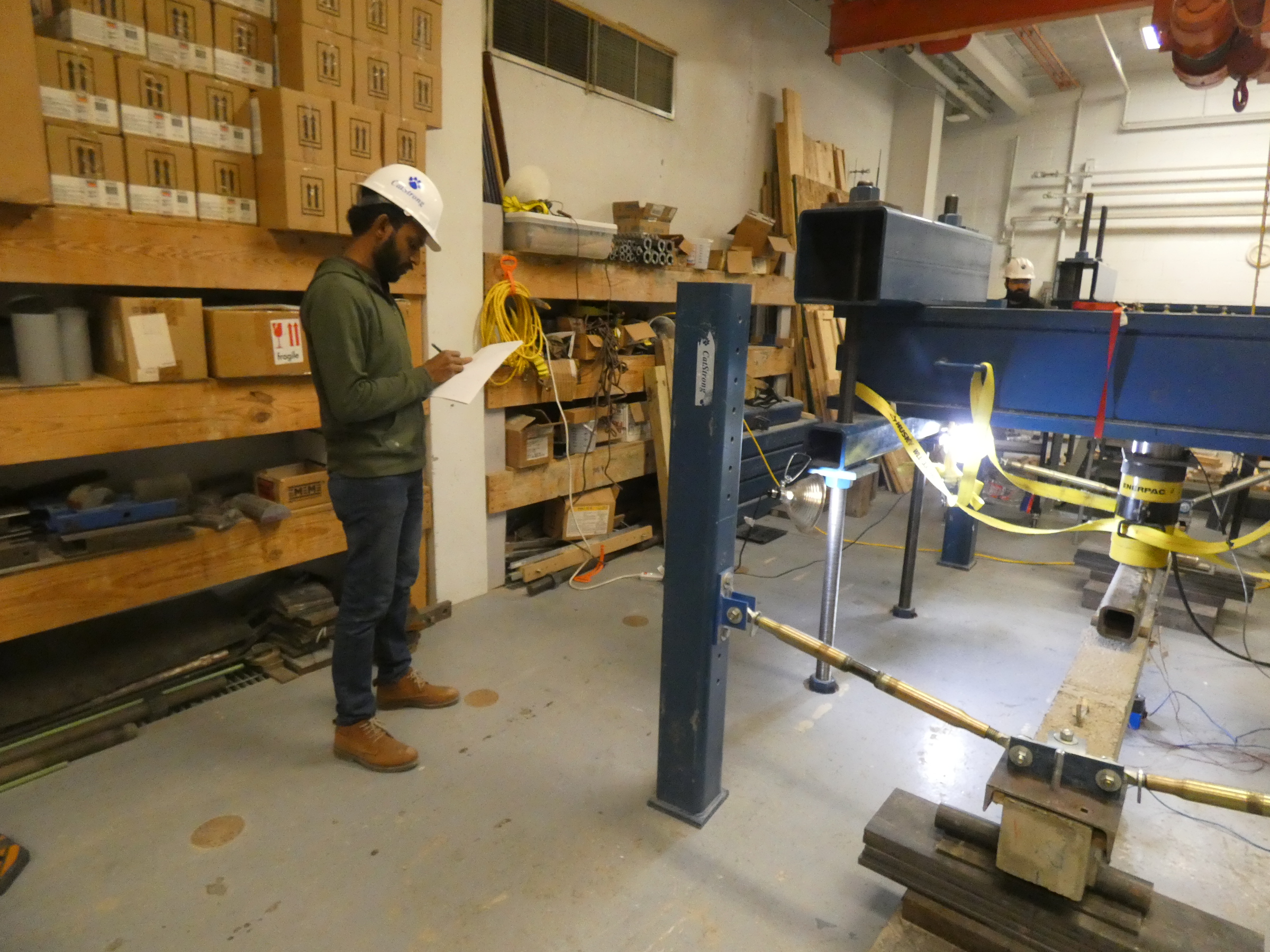Photos of student with writing pad in hand and wearing a hard hat observing a concrete beam test in the structure’s lab. 