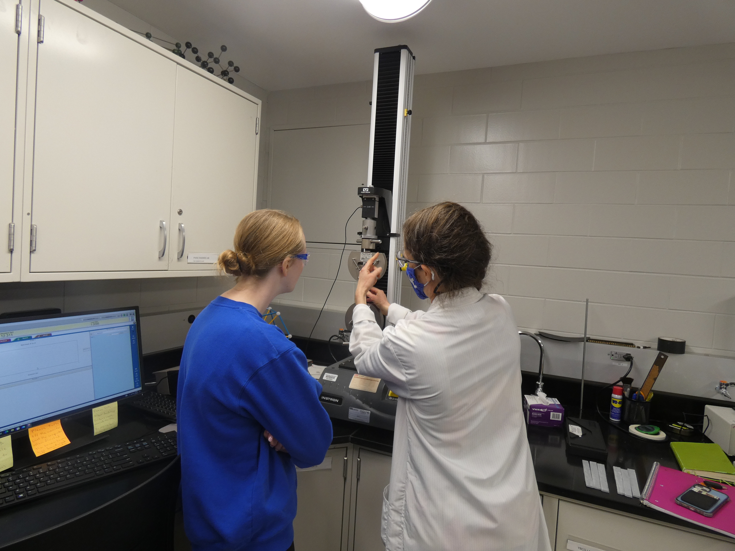 Photo of student with University of Kentucky Research Facility Manager in Chemical Engineering utilizing a small tensile testing machine to test epoxy specimen. 