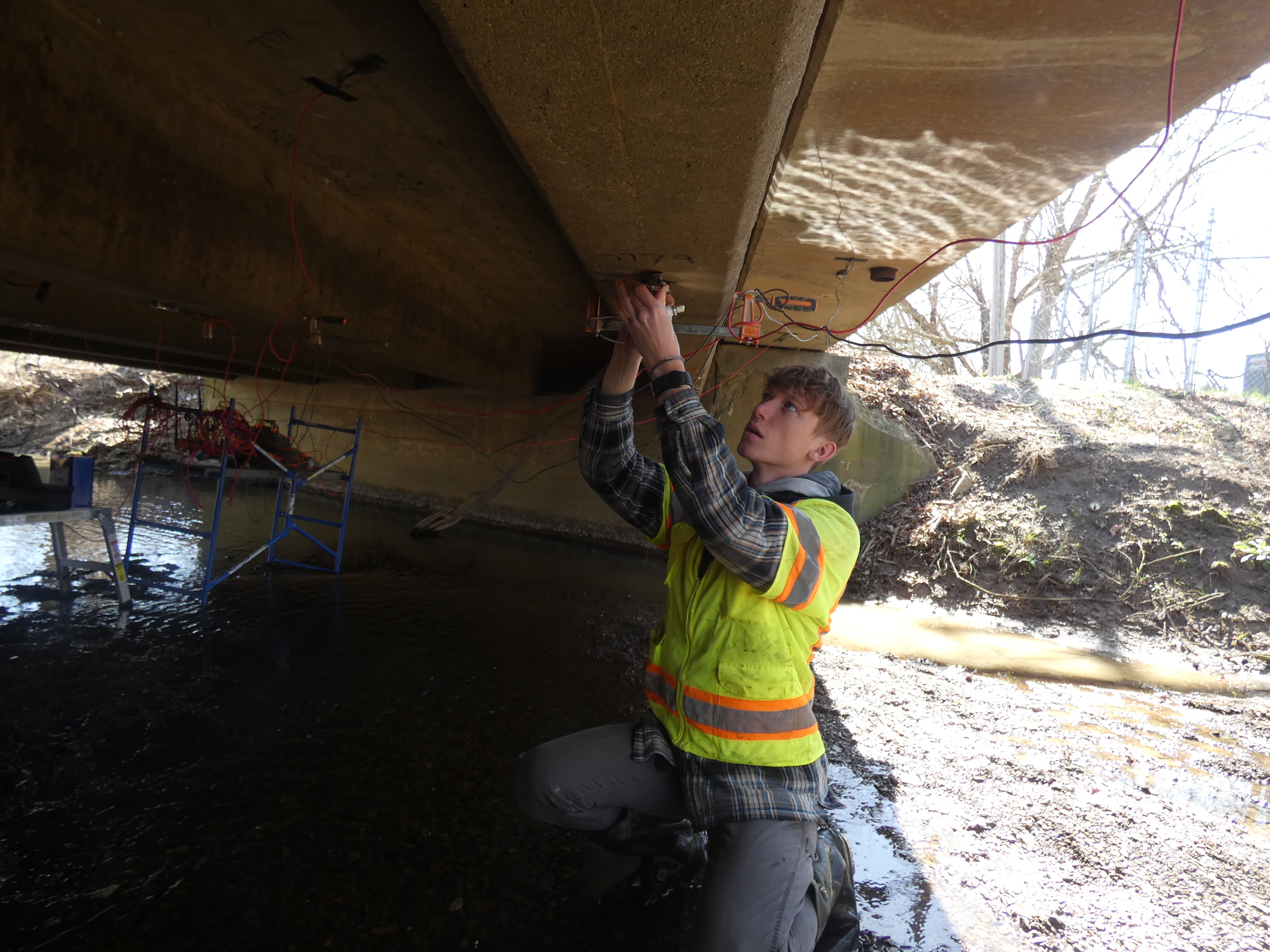 Photo of student applying a strain gauge on the bottom of beam in a reinforced concrete bridge.   