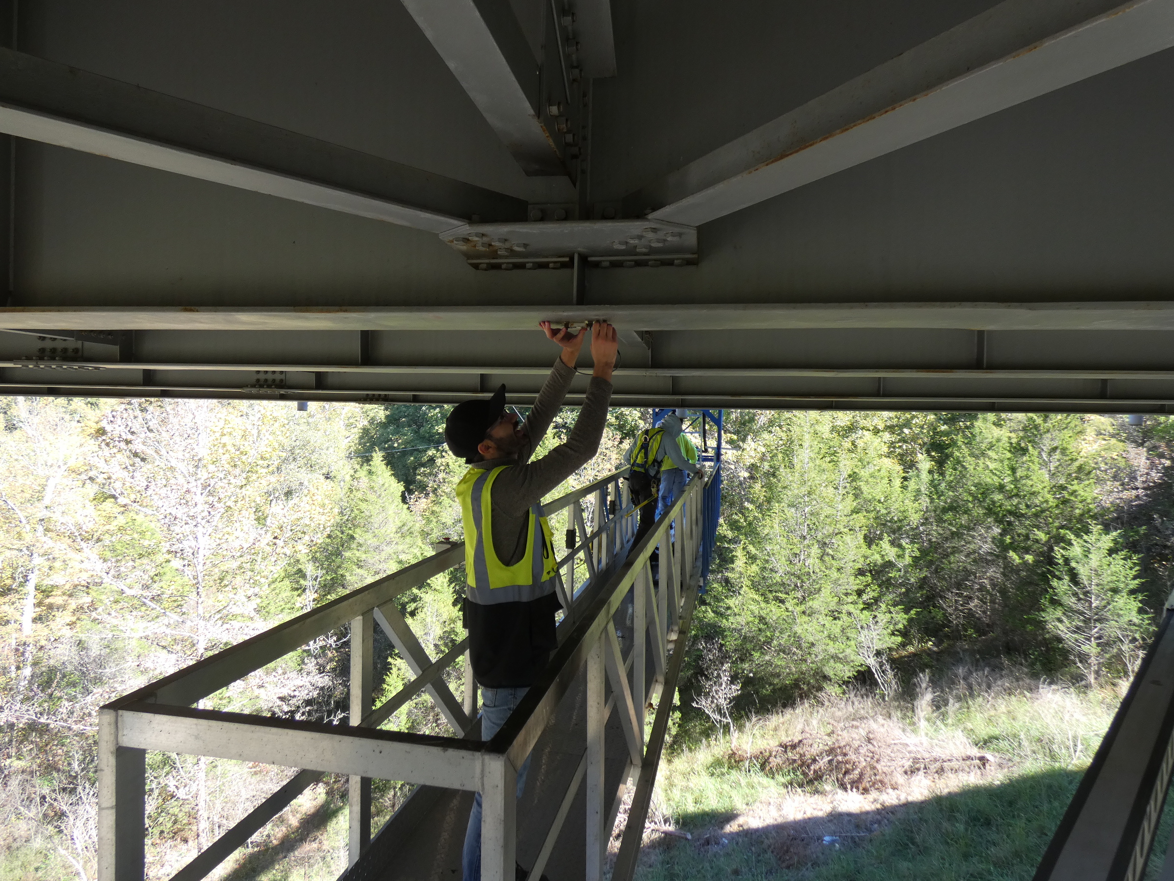 Photo of student applying a strain gauge on the bottom of beam in a steel girder bridge.  The student is working off a work platform.